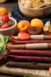 Photo of Tasty candied leather rolls, fruits and berries on wooden table, closeup