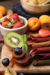 Photo of Tasty candied leather rolls, fruits and berries on wooden table, closeup