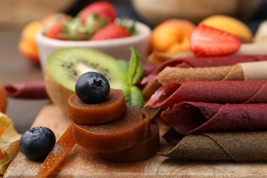Photo of Tasty candied leather rolls, fruits and berries on wooden table, closeup