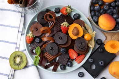Photo of Tasty candied leather rolls, fruits and berries on white table, flat lay