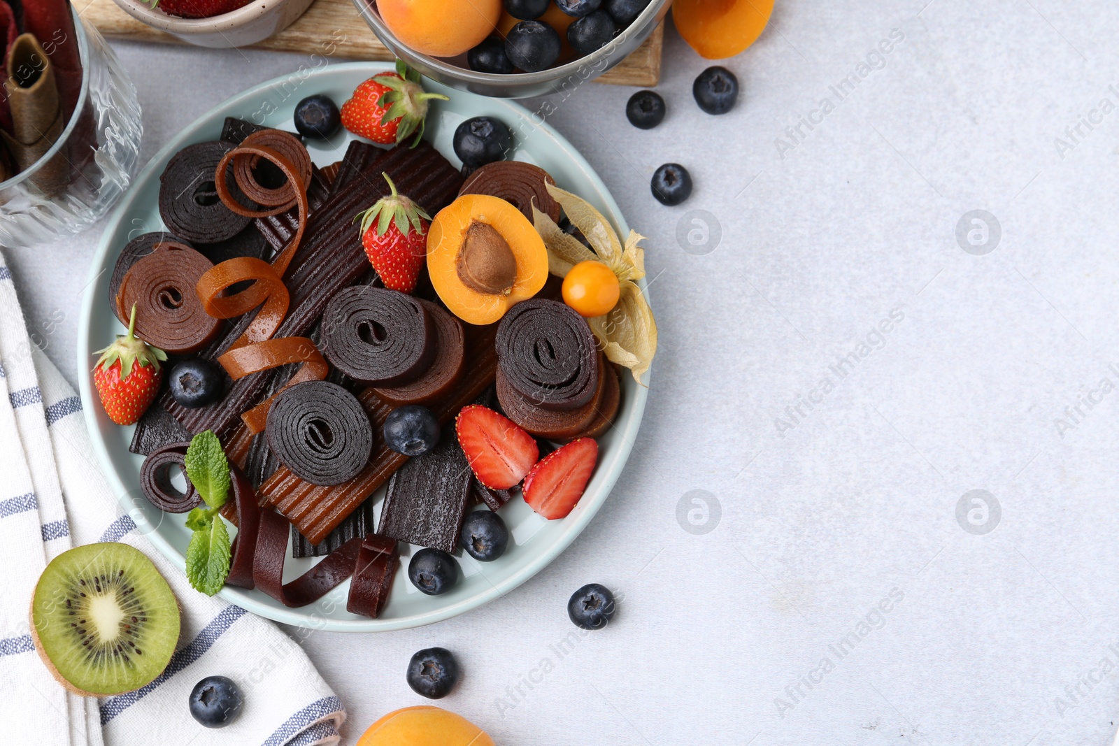 Tasty candied leather rolls, fruits and berries on white table, flat lay. Space for text Photo of Tasty candied leather rolls, fruits and berries on white table, flat lay. Space for text