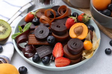 Photo of Tasty candied leather rolls, fruits and berries on white table, closeup