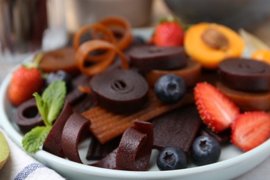 Photo of Tasty candied leather rolls, fruits and berries on white table, closeup