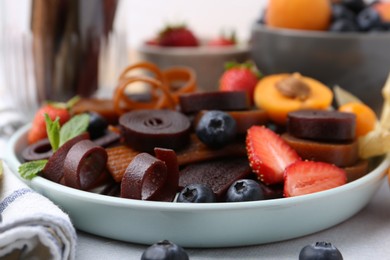 Photo of Tasty candied leather rolls, fruits and berries on white table, closeup