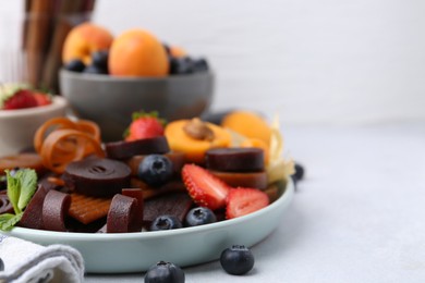 Photo of Tasty candied leather rolls, fruits and berries on white table, closeup. Space for text