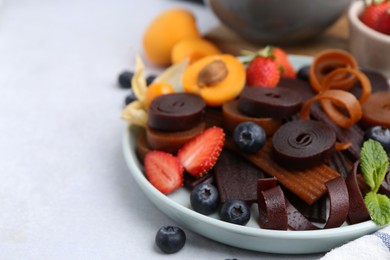 Photo of Tasty candied leather rolls, fruits and berries on white table, closeup. Space for text