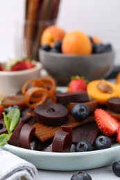 Photo of Tasty candied leather rolls, fruits and berries on white table, closeup