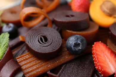 Photo of Tasty candied leather rolls, fruits and berries, closeup