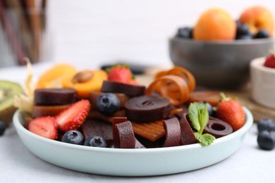 Photo of Tasty candied leather rolls, fruits and berries on white table, closeup