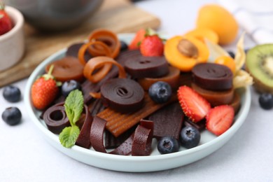 Photo of Tasty candied leather rolls, fruits and berries on white table, closeup