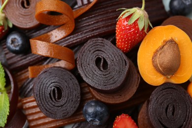 Photo of Tasty candied leather rolls, fruits and berries, closeup