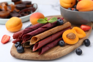 Photo of Tasty candied leather rolls, fruits and berries on white table, closeup