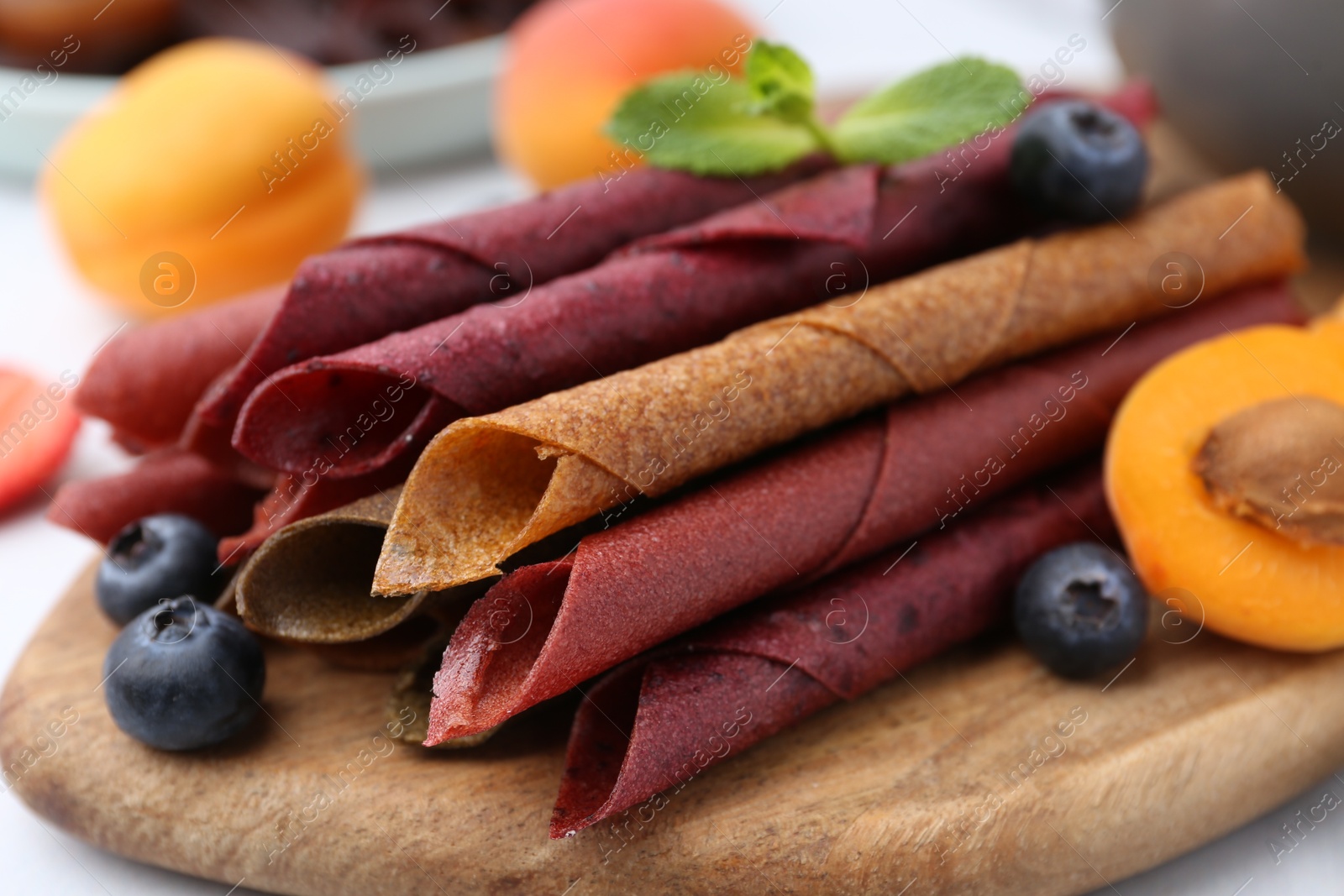 Tasty candied leather rolls, fruits and berries on white table, closeup Photo of Tasty candied leather rolls, fruits and berries on white table, closeup