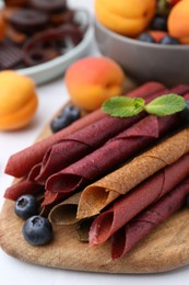 Photo of Tasty candied leather rolls, fruits and berries on white table, closeup