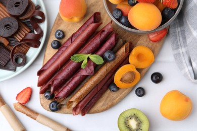 Photo of Tasty candied leather rolls, fruits and berries on white table, flat lay