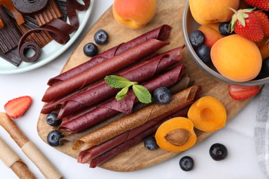 Photo of Tasty candied leather rolls, fruits and berries on white table, flat lay