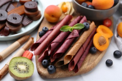 Photo of Tasty candied leather rolls, fruits and berries on white table, closeup