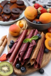 Photo of Tasty candied leather rolls, fruits and berries on white table, closeup