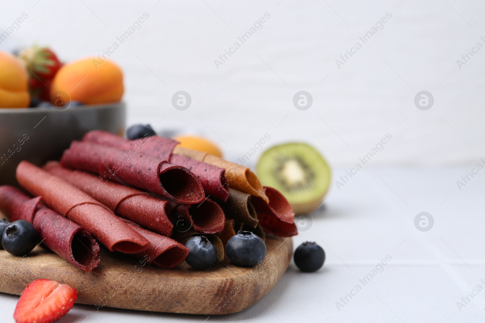 Tasty candied leather rolls, fruits and berries on white tiled table, closeup. Space for text Photo of Tasty candied leather rolls, fruits and berries on white tiled table, closeup. Space for text
