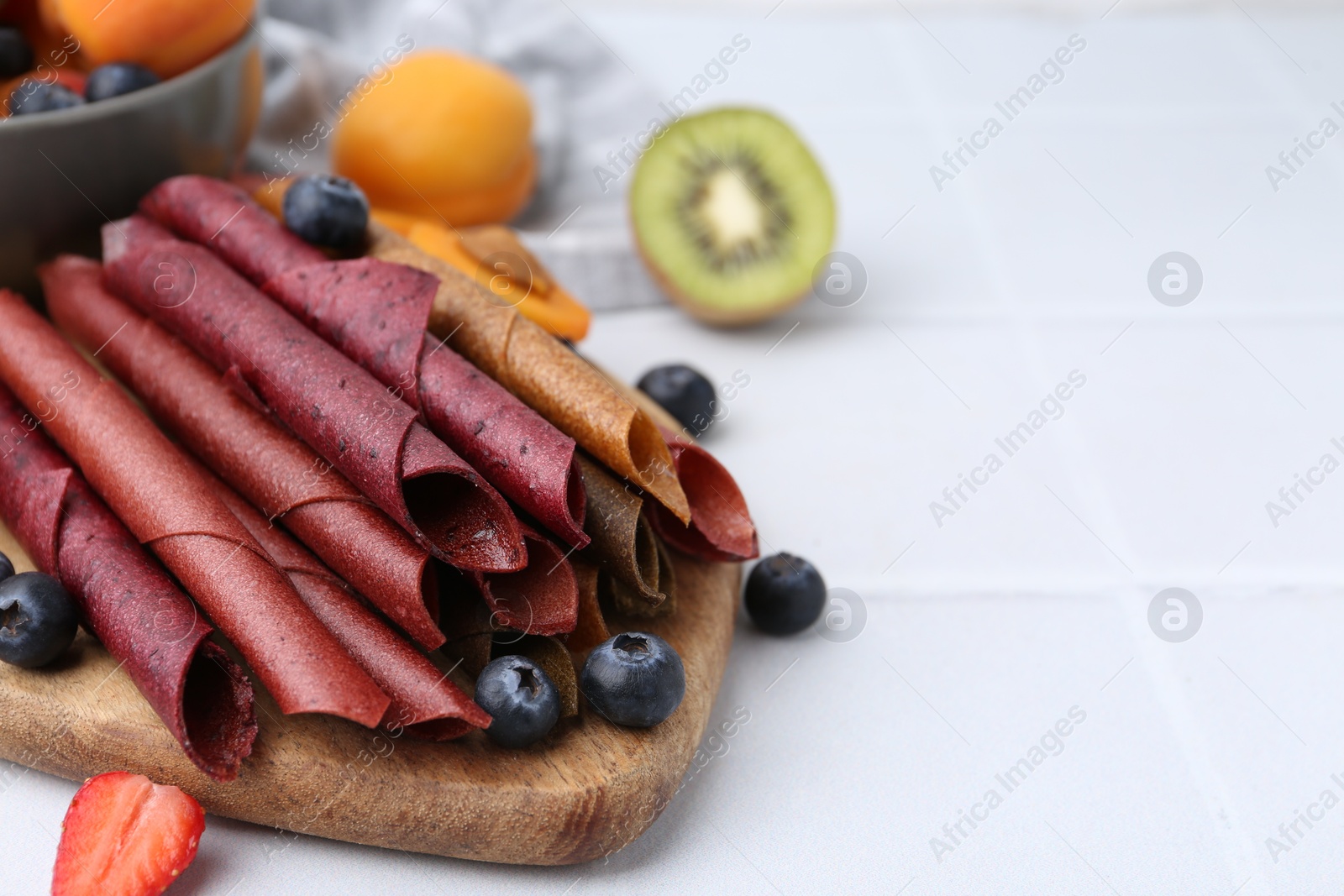 Tasty candied leather rolls, fruits and berries on white tiled table, closeup. Space for text Photo of Tasty candied leather rolls, fruits and berries on white tiled table, closeup. Space for text