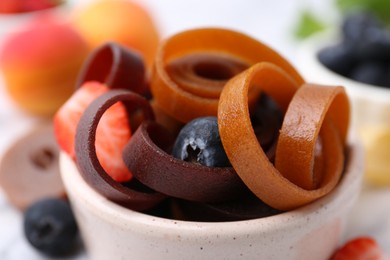 Photo of Tasty fruit leather rolls in bowl and berries on table, closeup