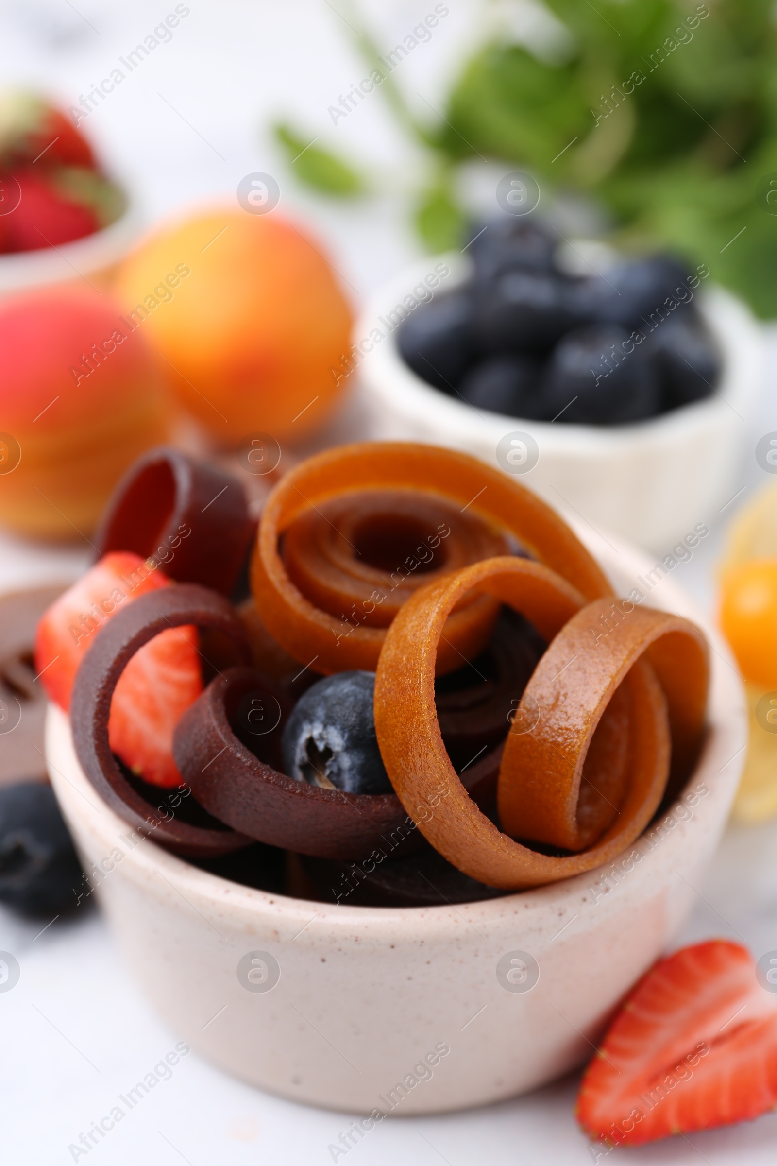 Tasty fruit leather rolls in bowl and berries on white marble table, closeup Photo of Tasty fruit leather rolls in bowl and berries on white marble table, closeup