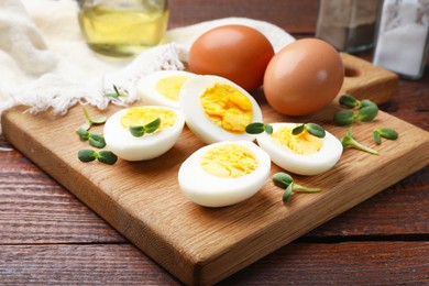 Photo of Halves of hard boiled eggs with microgreens on wooden table, closeup