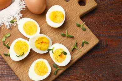 Photo of Halves of hard boiled eggs with microgreens on wooden table, top view