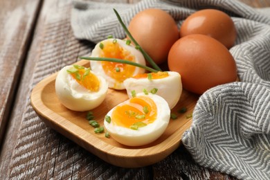 Photo of Soft boiled eggs with green onions on wooden table, closeup