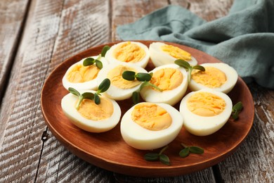Photo of Hard boiled eggs with microgreens on wooden table, closeup