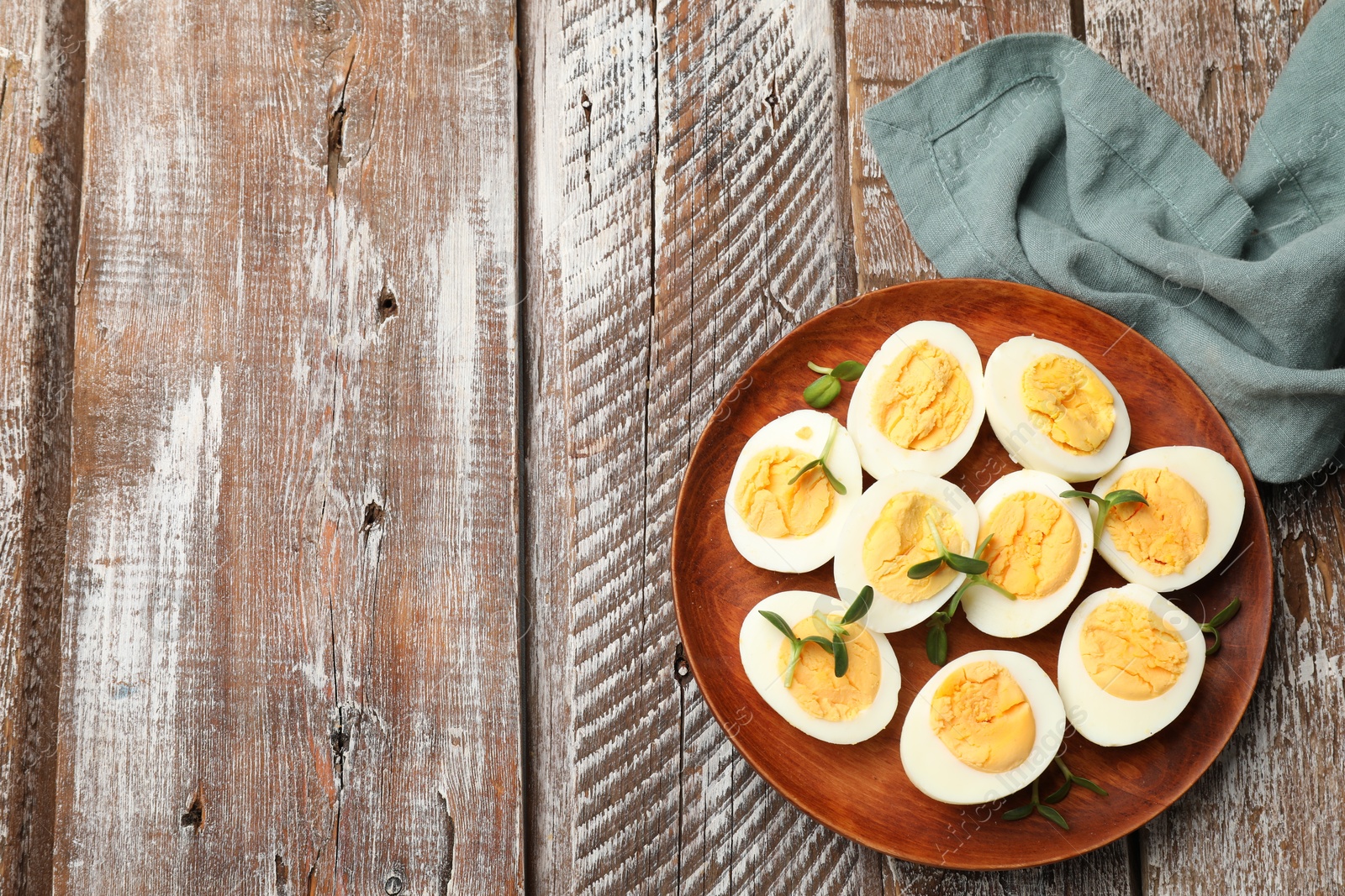 Photo of Hard boiled eggs with microgreens on wooden table, top view. Space for text