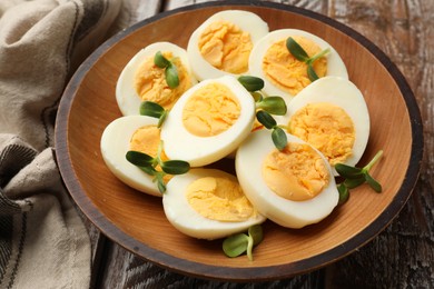 Photo of Hard boiled eggs with microgreens on wooden table, closeup