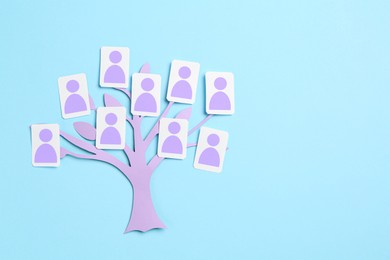 Image of Family tree. Cards with human icons attached to paper tree on light blue background, top view. Space for text