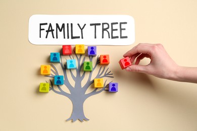 Image of Family tree. Woman putting cube with human icon to composition with paper tree on beige background, top view