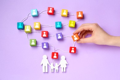 Image of Woman putting cube with human icon to composition of other cubes, rope and figure of family on violet background, top view