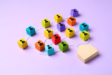 Image of Colorful cubes with human icons on white rope leading to wooden house figure on violet background. Family ties composition