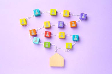Image of Colorful cubes with human icons on white rope leading to wooden house figure on violet background, top view. Family ties composition
