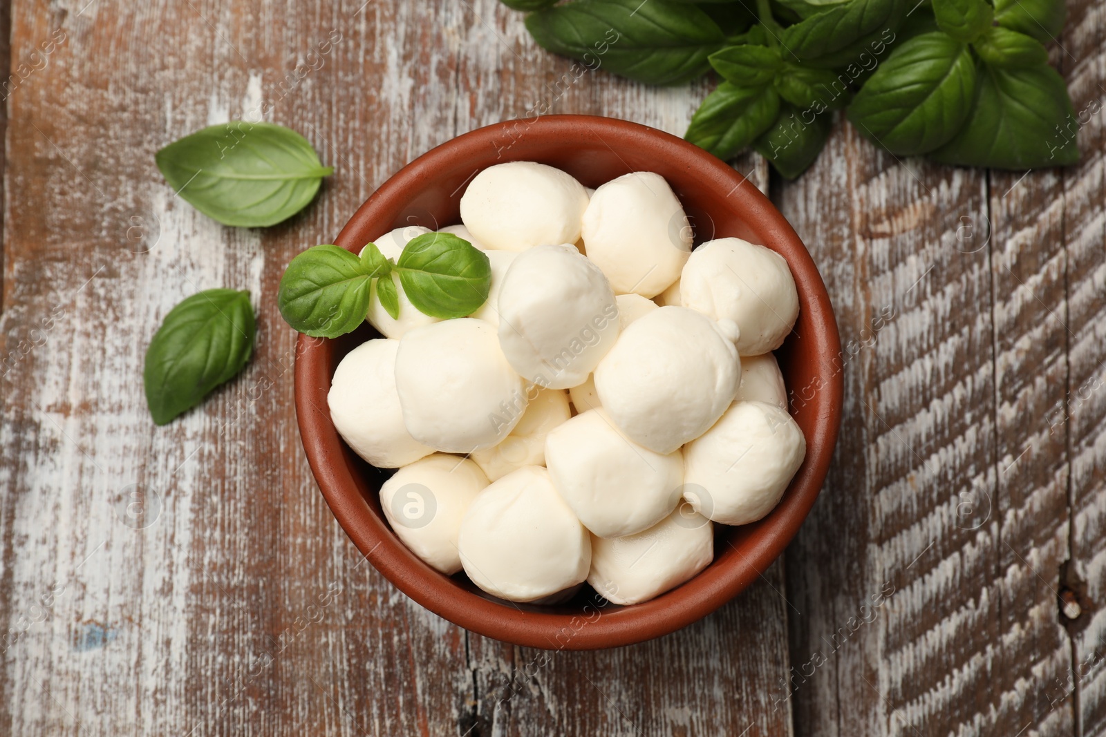 Tasty mozzarella cheese balls in bowl and basil on wooden table, flat lay Photo of Tasty mozzarella cheese balls in bowl and basil on wooden table, flat lay