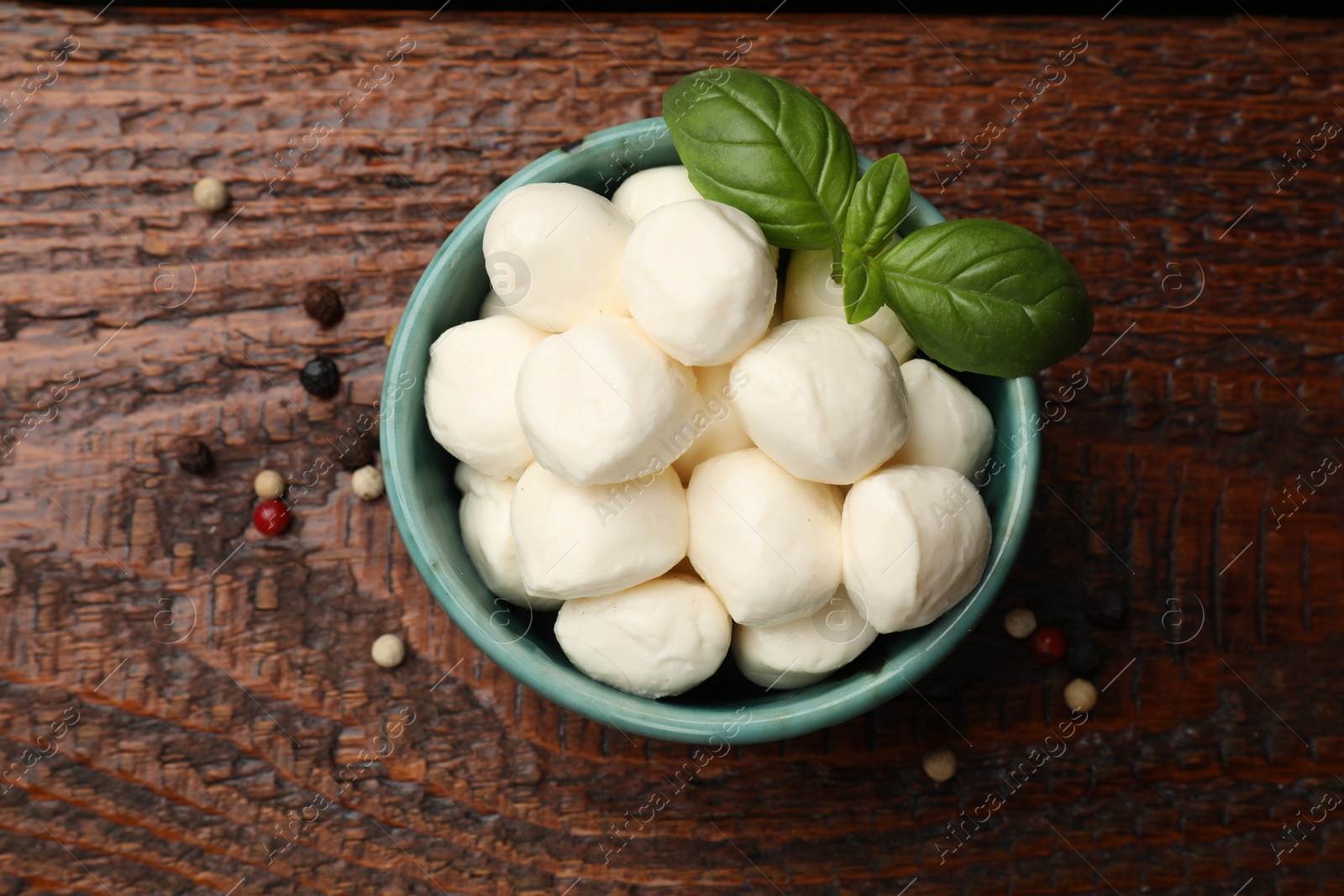 Tasty mozzarella cheese balls in bowl, peppercorns and basil on wooden table, top view Photo of Tasty mozzarella cheese balls in bowl, peppercorns and basil on wooden table, top view