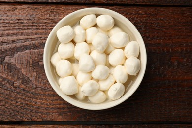 Photo of Tasty mozzarella cheese balls in bowl on wooden table, top view