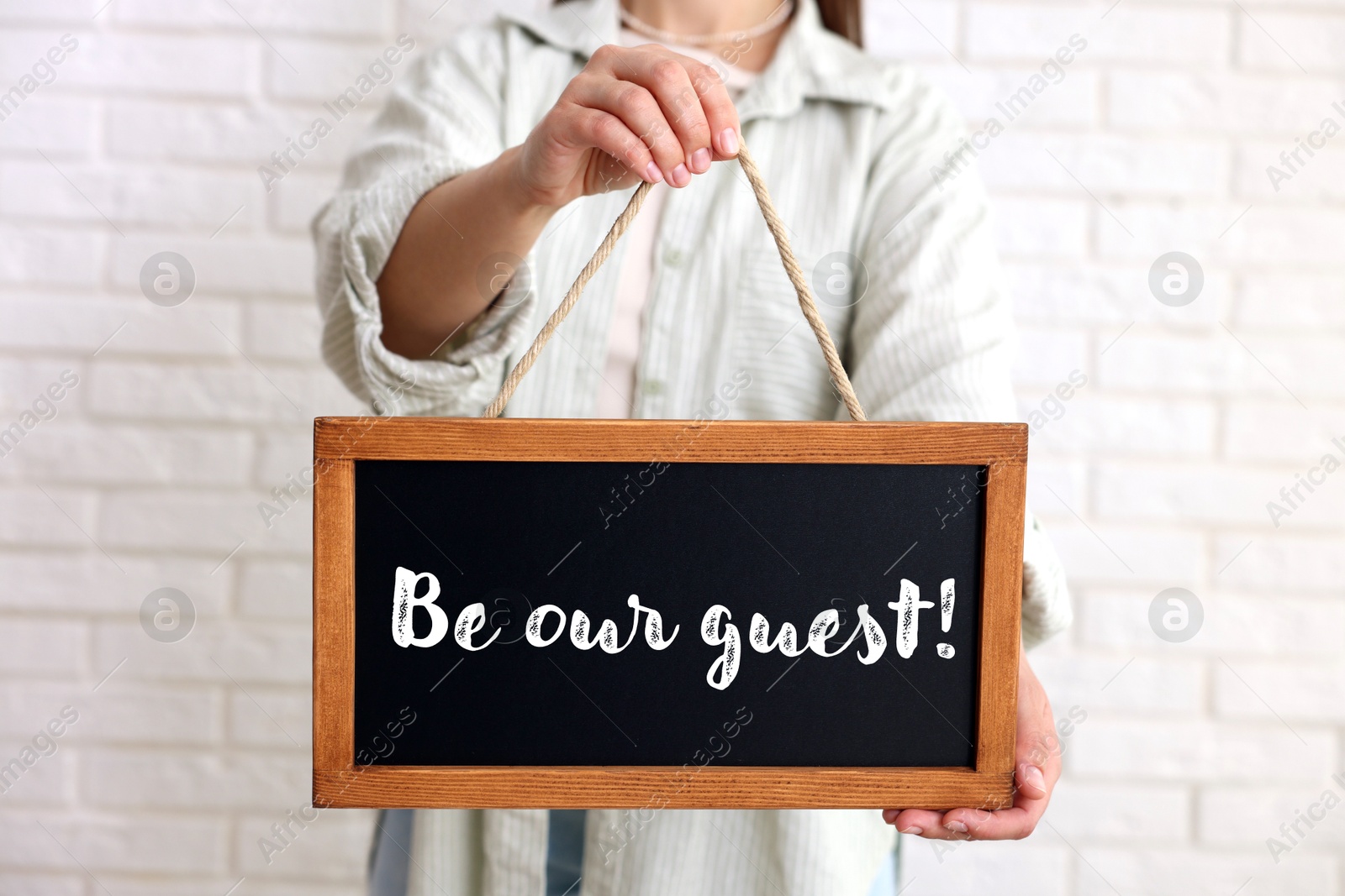 Woman holding small blackboard with phrase Be Our Guest indoors, closeup Image of Woman holding small blackboard with phrase Be Our Guest indoors, closeup