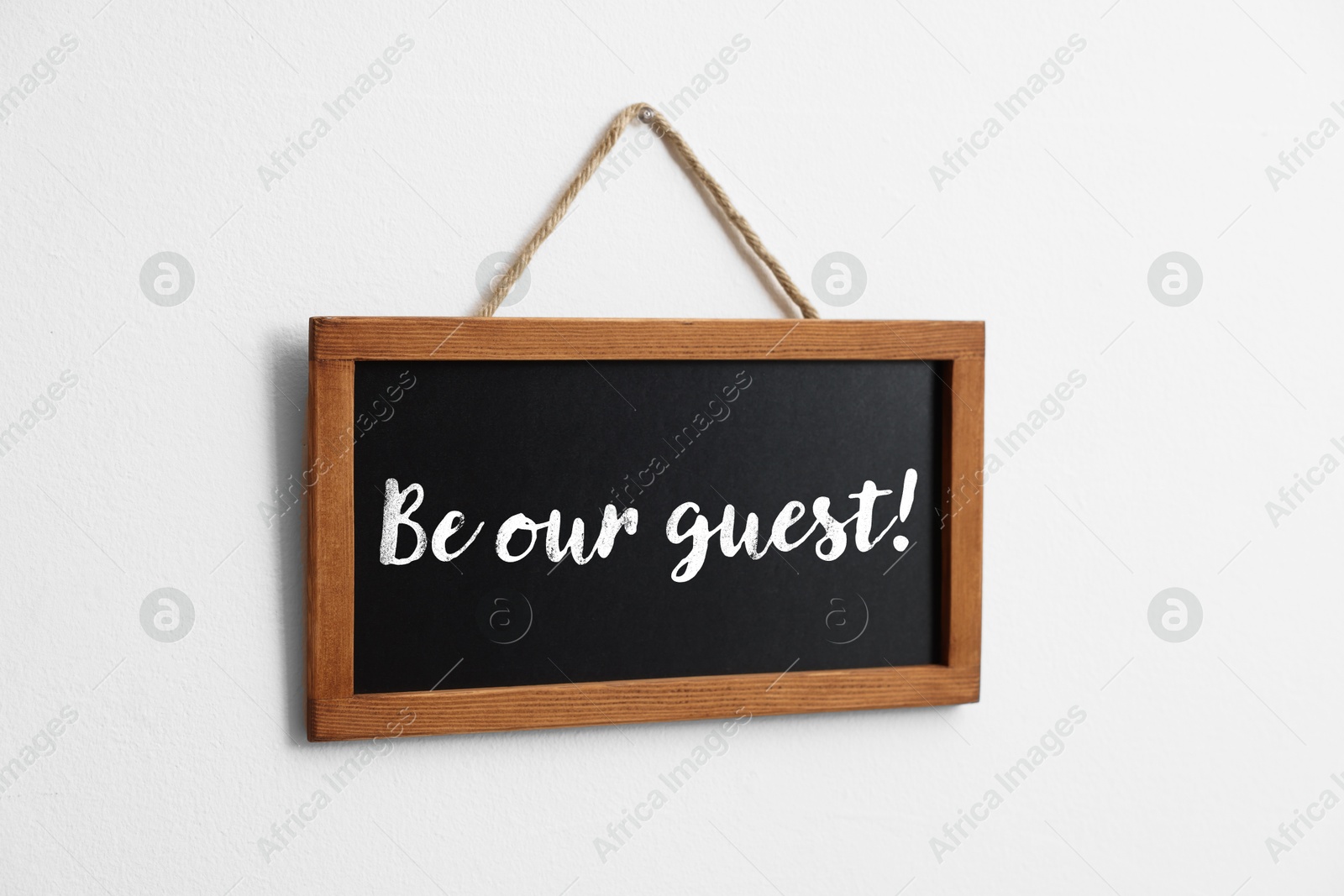 Small blackboard with phrase Be Our Guest hanging on white wall Image of Small blackboard with phrase Be Our Guest hanging on white wall