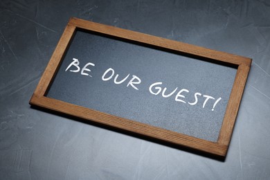 Image of Small blackboard with phrase Be Our Guest on dark gray textured background, above view