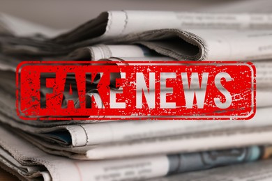 Image of Red Fake News stamp and newspapers on table, closeup