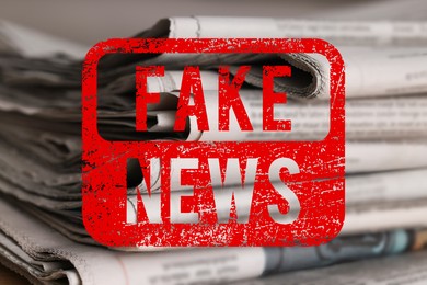 Image of Red Fake News stamp and newspapers on table, closeup
