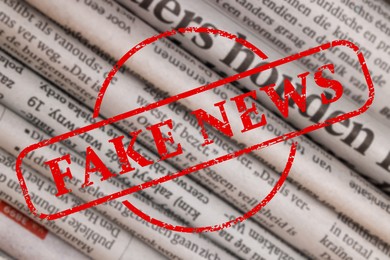 Image of Red Fake News stamp and newspapers in different languages as background, closeup