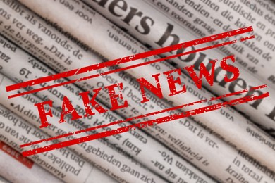 Image of Red Fake News stamp and newspapers in different languages as background, closeup