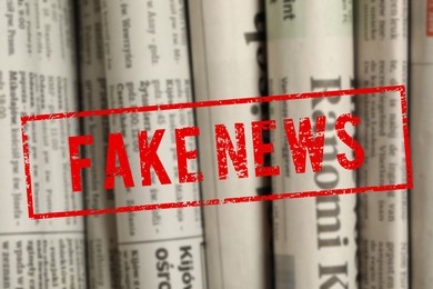 Image of Red Fake News stamp and newspapers in different languages as background, closeup