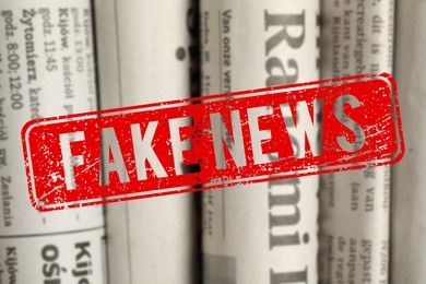 Image of Red Fake News stamp and newspapers in different languages as background, closeup