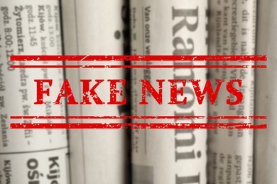 Image of Red Fake News stamp and newspapers in different languages as background, closeup